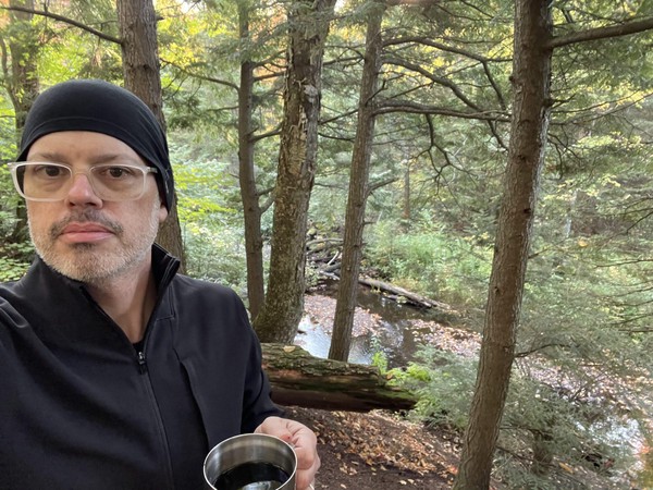 Me in a jacket and hat having my morning coffee above the Little Carp River