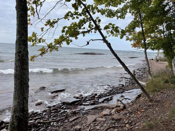 A rocky shore of Lake Superior with a small wave coming in and a few trees in the middle ground