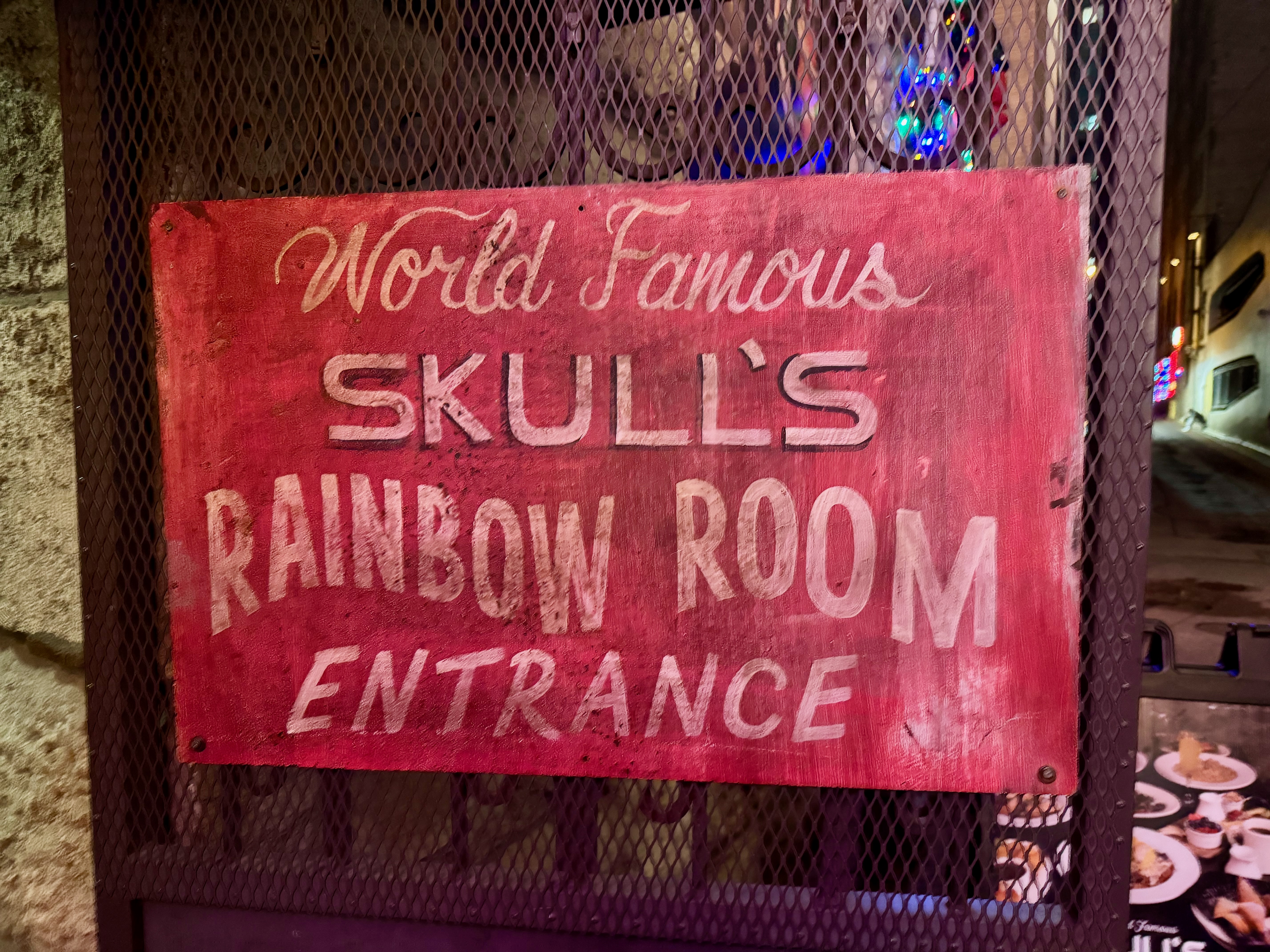 An old hand-painted sign that reads “World Famous Skull’s Rainbow Room Entrance”