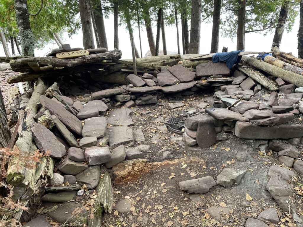 Fire pit with makeshift stone furniture surrounding it. Trees & Lake Superior in the background.
